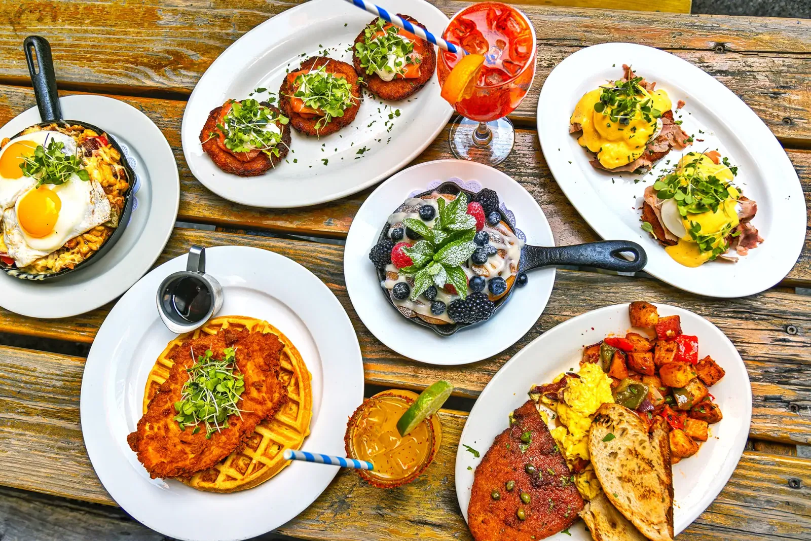 A brunch table covered in plates of eggs, waffles, shakshuka and cocktails, seen from above