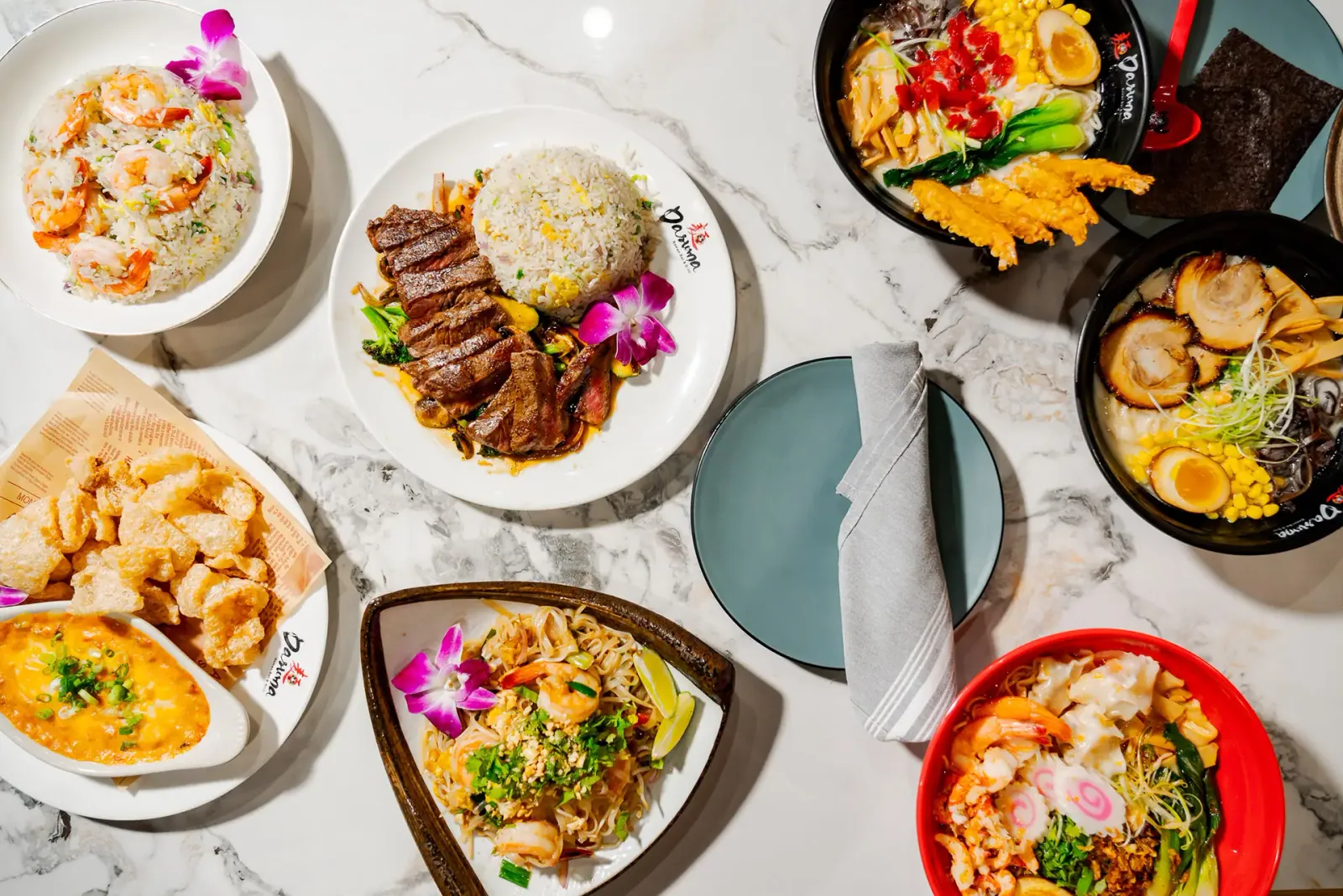 Top-down spread of Japanese rice bowls with steak, spicy tuna and shrimp on a marble table