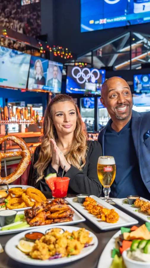 Guests toasting with drinks and pizza at a sports bar