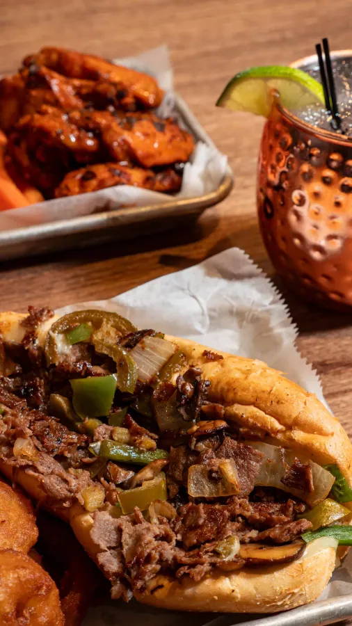 Cheesesteak sandwich with peppers and onions next to a copper mug