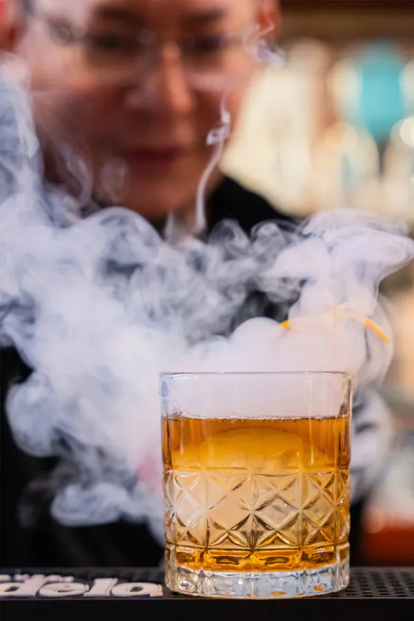 Smoked cocktail in a rocks glass under a cloud of smoke