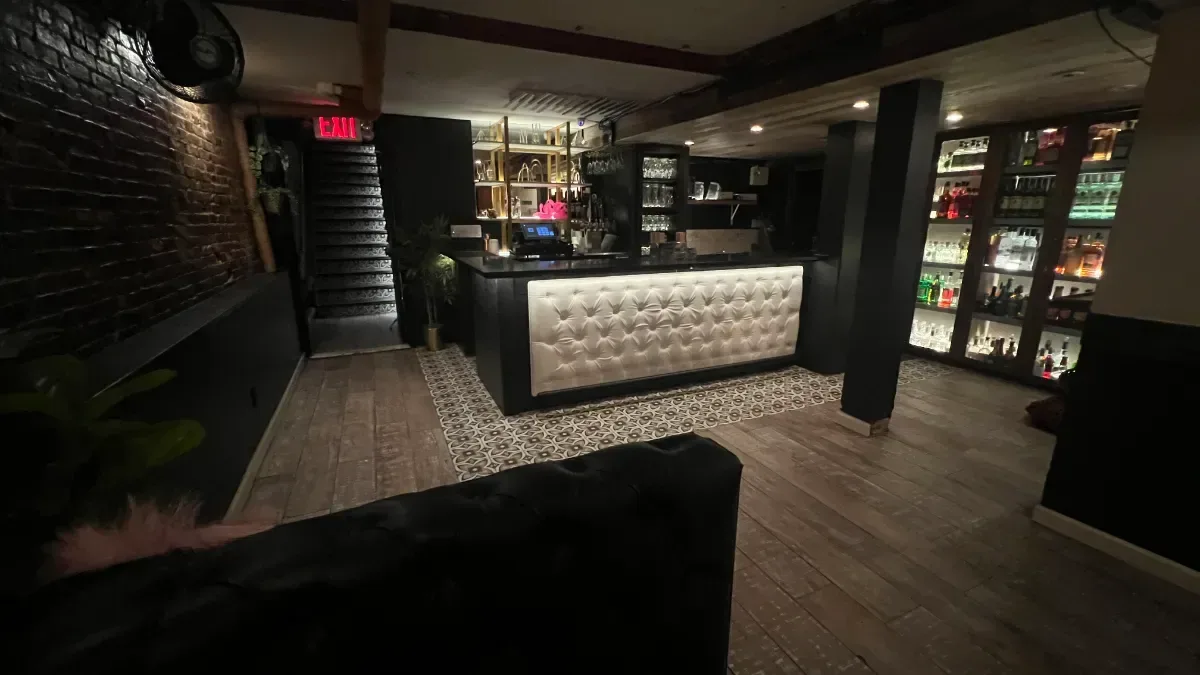 The private bar in the party room at Loreley Beer Garden, a tufted white bar front and lit shelves of bottles