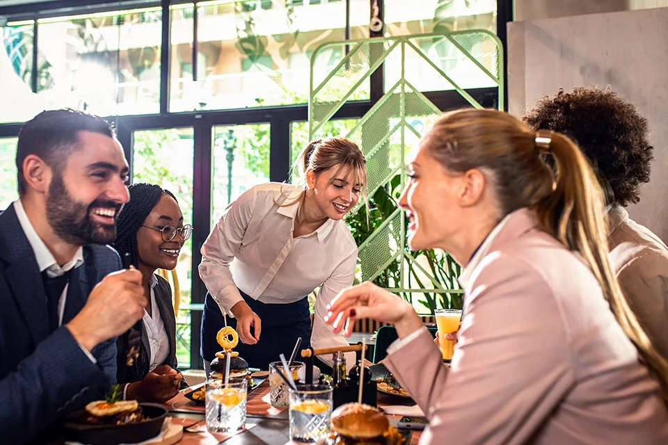 Guests laughing at a table while a server pours drinks