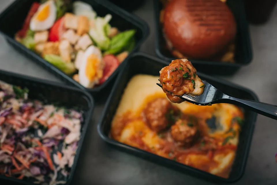 Takeout containers of salad, meatballs and a burger