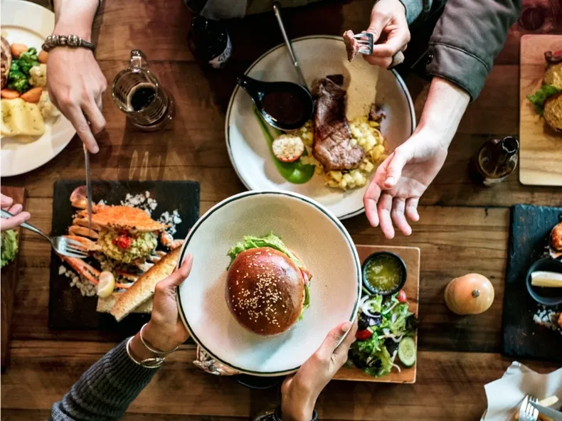 Friends sharing burgers, steak and crab at a wooden table