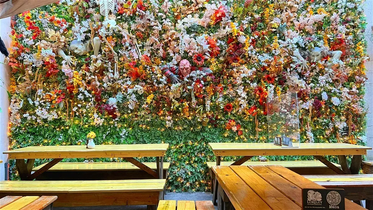 The flower wall at Loreley Beer Garden in fall colors with skeletons and masks in the flowers, above wooden picnic tables