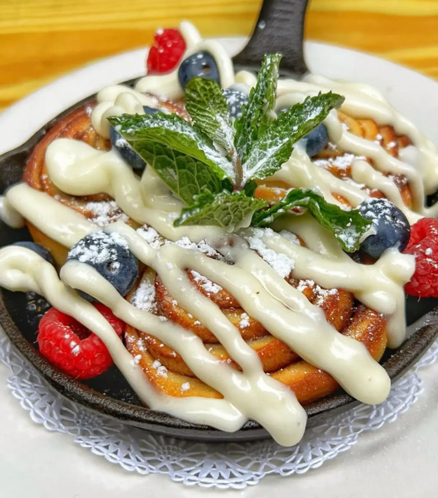 Skillet of cinnamon rolls drizzled with icing, topped with fresh berries and mint